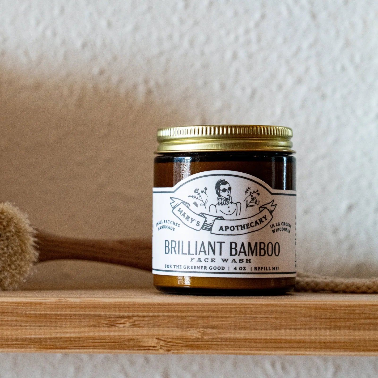 Jar of 'Brilliant Bamboo' face wash on a wooden shelf with a scrubber in the background.