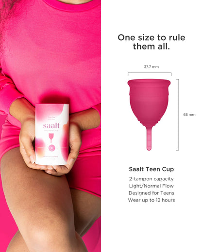 Person holding a Saalt Teen Cup packaging with product details on a pink background