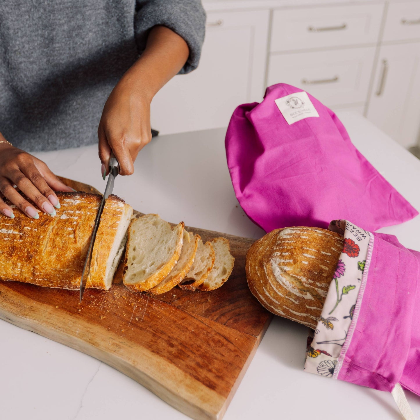 Person slicing bread on a wooden cutting board with pink bread bag.